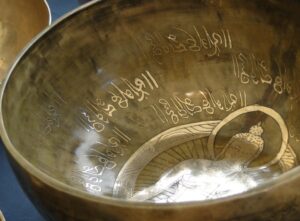 Bronze bowl with a carved Buddha figure inside and decorative script along the inner wall.