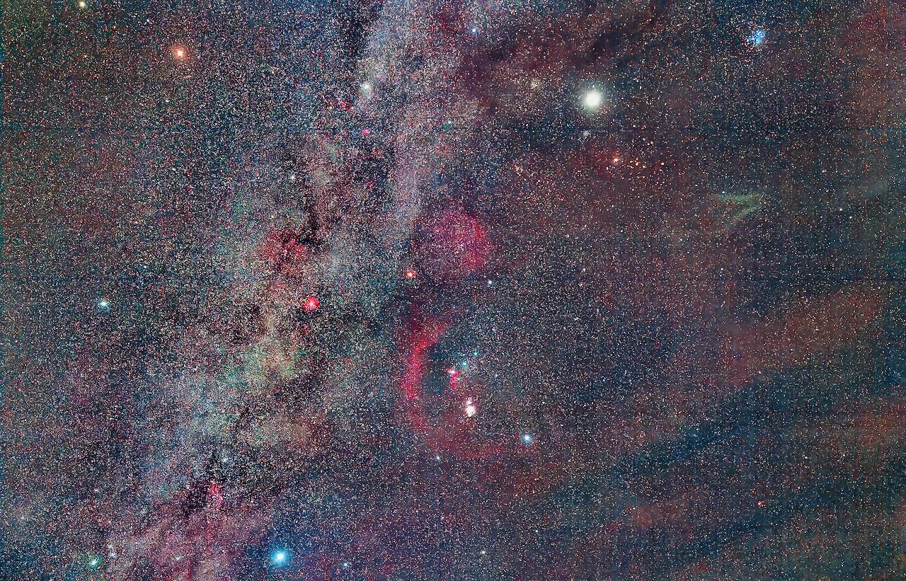 Wide field image of a colorful nebula with dust lanes and a dense field of stars in red, blue, and green hues.