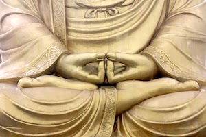 Close-up of a golden Buddha statue's hands in meditation mudra, resting in the lap.