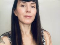 foto-claudia – Yoga vita e Salute Close-up portrait of a woman with long dark hair and a septum piercing, wearing a patterned sleeveless top, looking at the camera with a subtle smile.